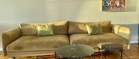 A beige sofa with patterned pillows, a small round table, and a chair in a room with wooden flooring.