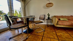 Ein Zimmer mit Holzdielenboden, einem runden Tisch mit Stühlen, einer Couch, einer Hängelampe und einer Kaktuspflanze.