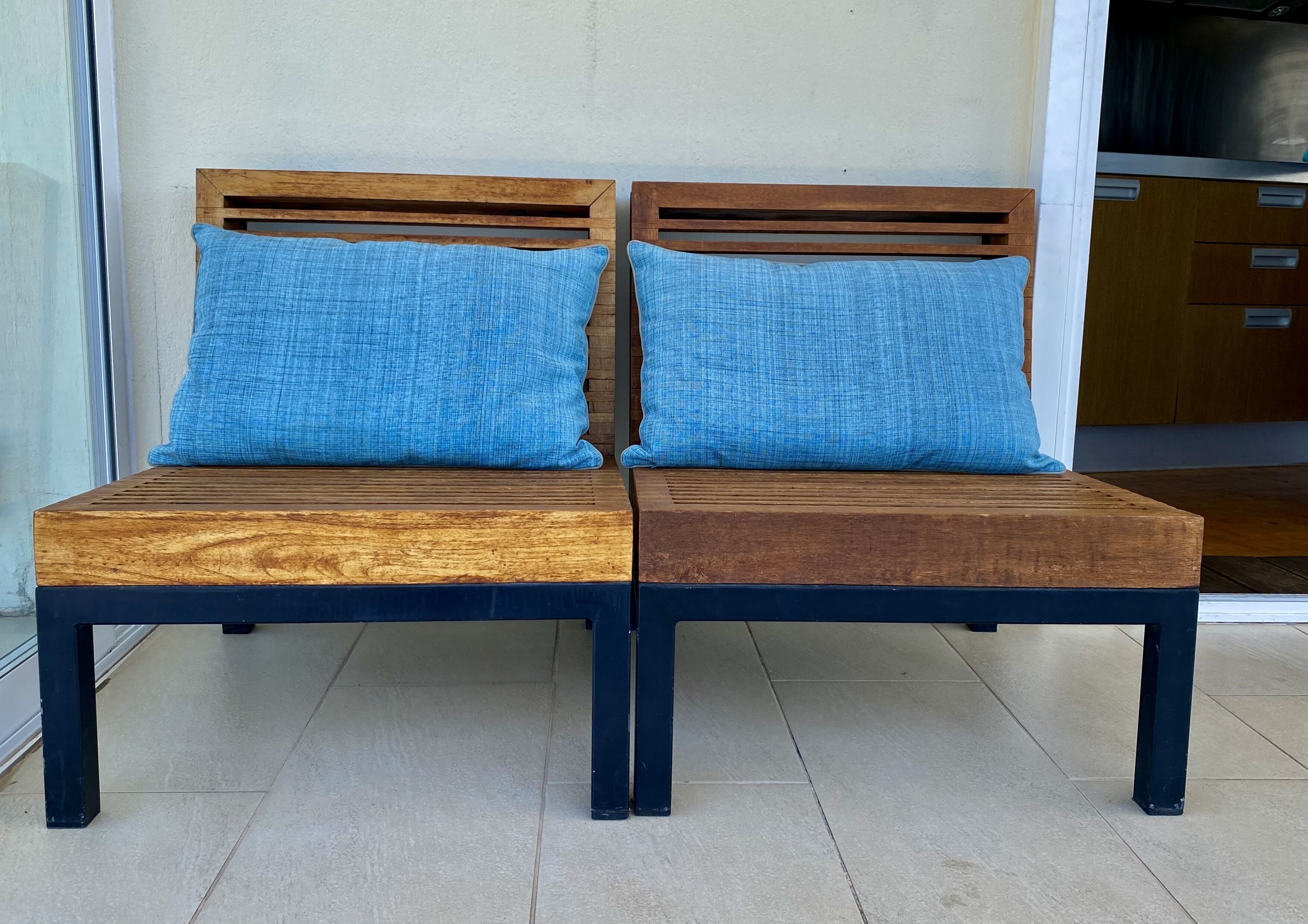 A wooden bench with two blue cushions, positioned in front of a wall with a window and a door.
