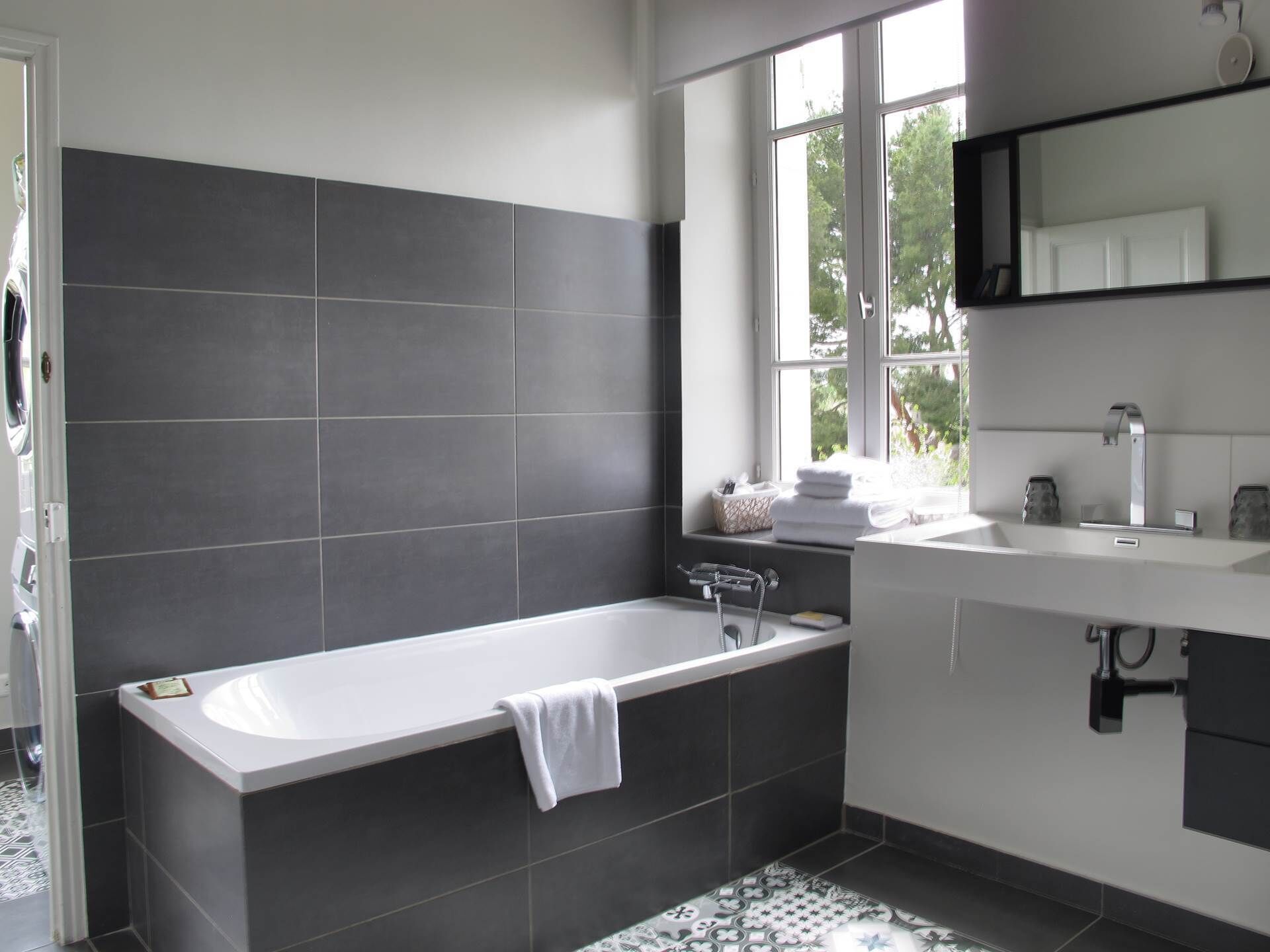A modern bathroom with a freestanding bathtub, a window with a view of greenery, and a white vanity with a mirror.