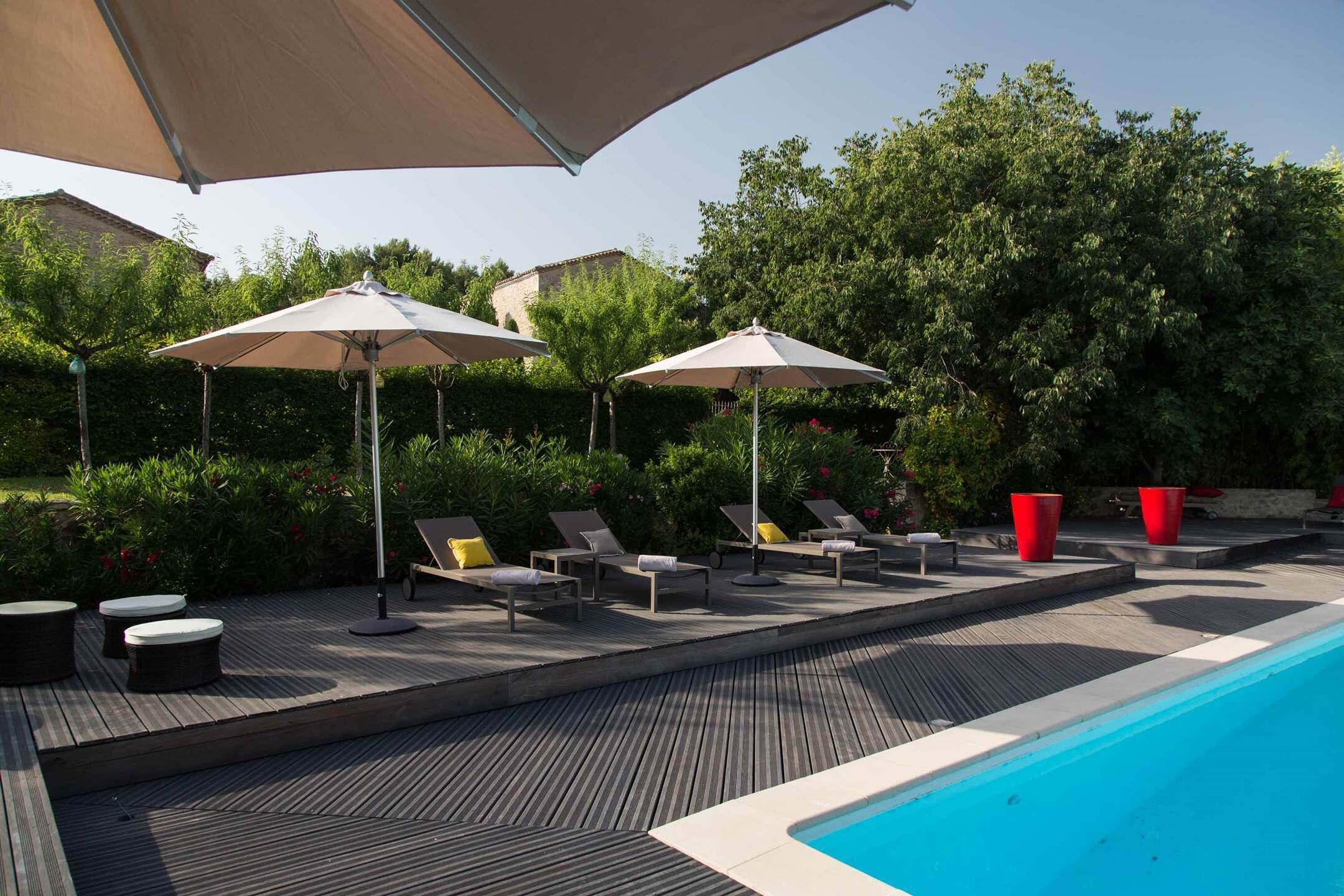 Área de piscina com espreguiçadeiras e guarda-sóis, cercada por vegetação e uma piscina azul cristalina.