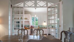 Un coin repas avec une table et des chaises en bois, une cuisine avec des meubles blancs et une fenêtre, et un lustre.