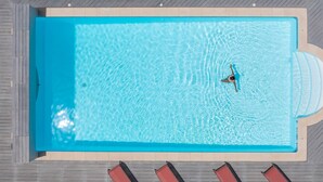 Une piscine rectangulaire à l’eau d’un bleu cristallin, entourée d’une terrasse en bois et de chaises longues rouges.