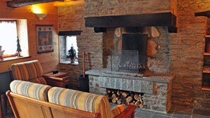 A cozy cabin interior with a stone fireplace, wooden furniture, and a log storage area. - A breath of fresh air in Normandy (Condé-En-Normandie)
