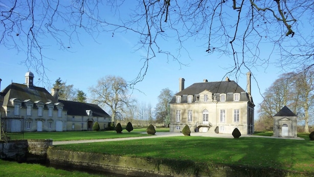 Een groot, historisch pand met een symmetrische gevel, een centrale ingang met een trap en een verzorgd gazon.