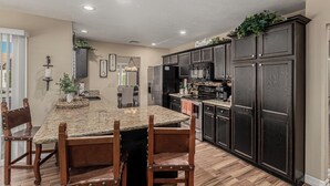 A modern kitchen with dark wood cabinets, a granite island, and a dining area with wooden chairs. - Scottsdale Escape - Close to Kierland All 5 star reviews !  Fall Savings! (Scottsdale)