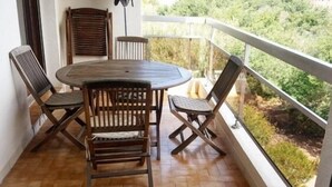 Ein Balkon mit einem Holztisch und Stühlen, einem weißen Geländer und Blick auf Grünflächen.