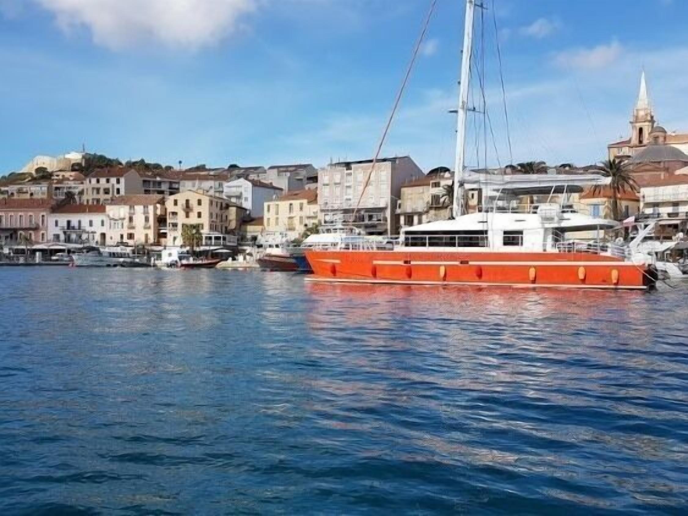 Ein großes, oranges Boot liegt im Hafen, im Hintergrund sind Gebäude und eine Kirche zu sehen.