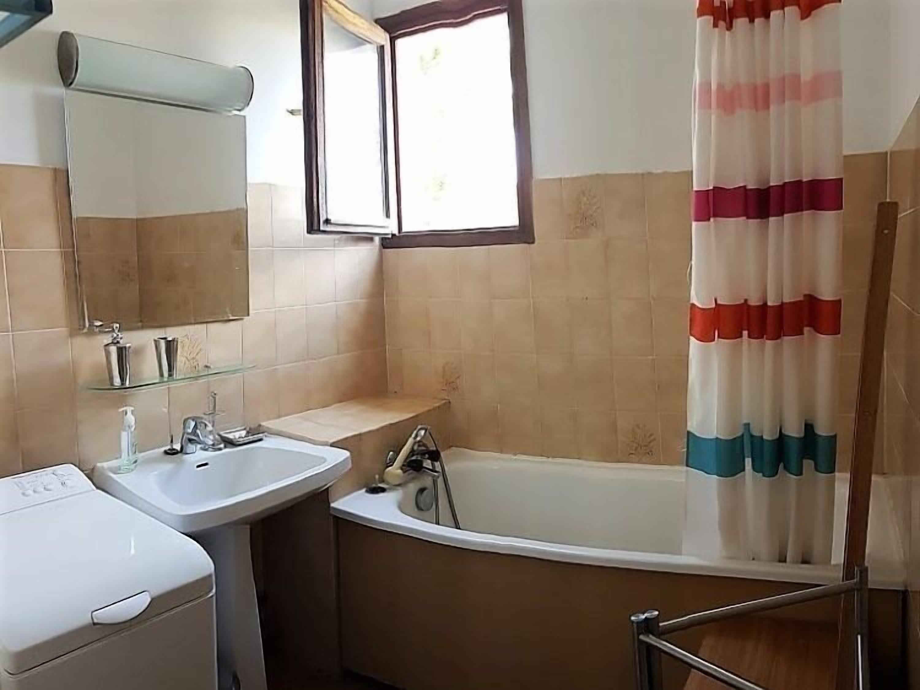 A bathroom with a bathtub, a sink, a mirror, and a window.