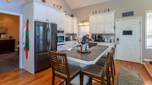 Una cocina con armarios blancos, un refrigerador de acero inoxidable y una zona de comedor con sillas de madera.