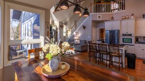 Una cocina amplia con armarios blancos, un comedor con mesa y sillas de madera, y una escalera que sube a un nivel superior.