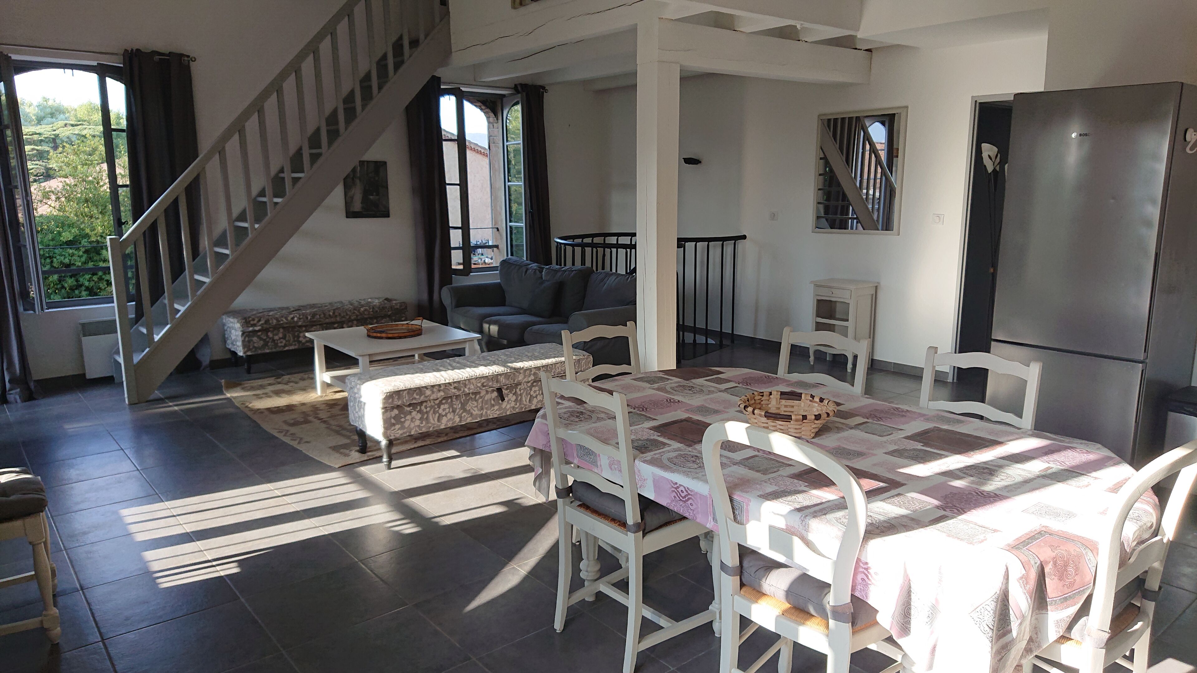 Un grand espace de vie comprenant un escalier, un canapé, une table à manger et un réfrigérateur.