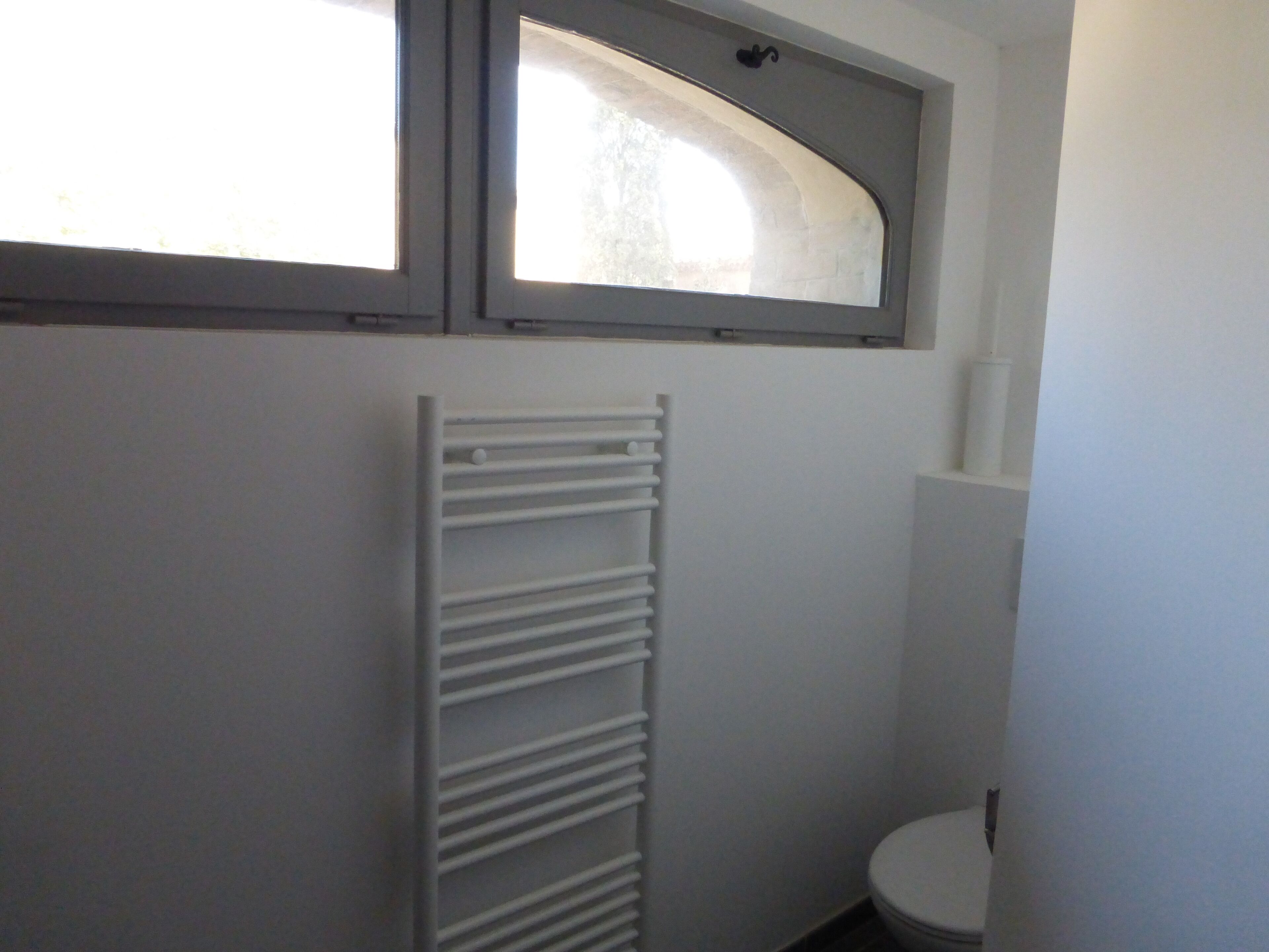 A small bathroom with a white toilet, a towel rack, and a window above the toilet.