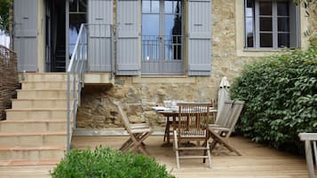 Un bâtiment en pierre doté d’une terrasse en bois, d’une table avec des chaises et d’un escalier.