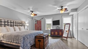Ein Schlafzimmer mit Bett, Koffer, Kommode, Spiegel und Deckenventilator.