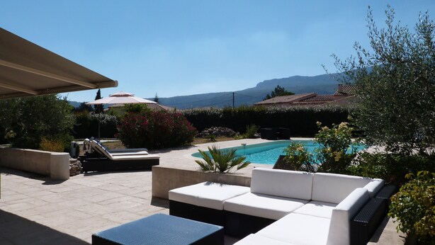 Une terrasse extérieure avec une piscine, des meubles de jardin blancs et une vue sur les montagnes.