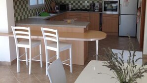 Une cuisine compacte avec un îlot central, deux chaises blanches, une table à manger et un vase vert.