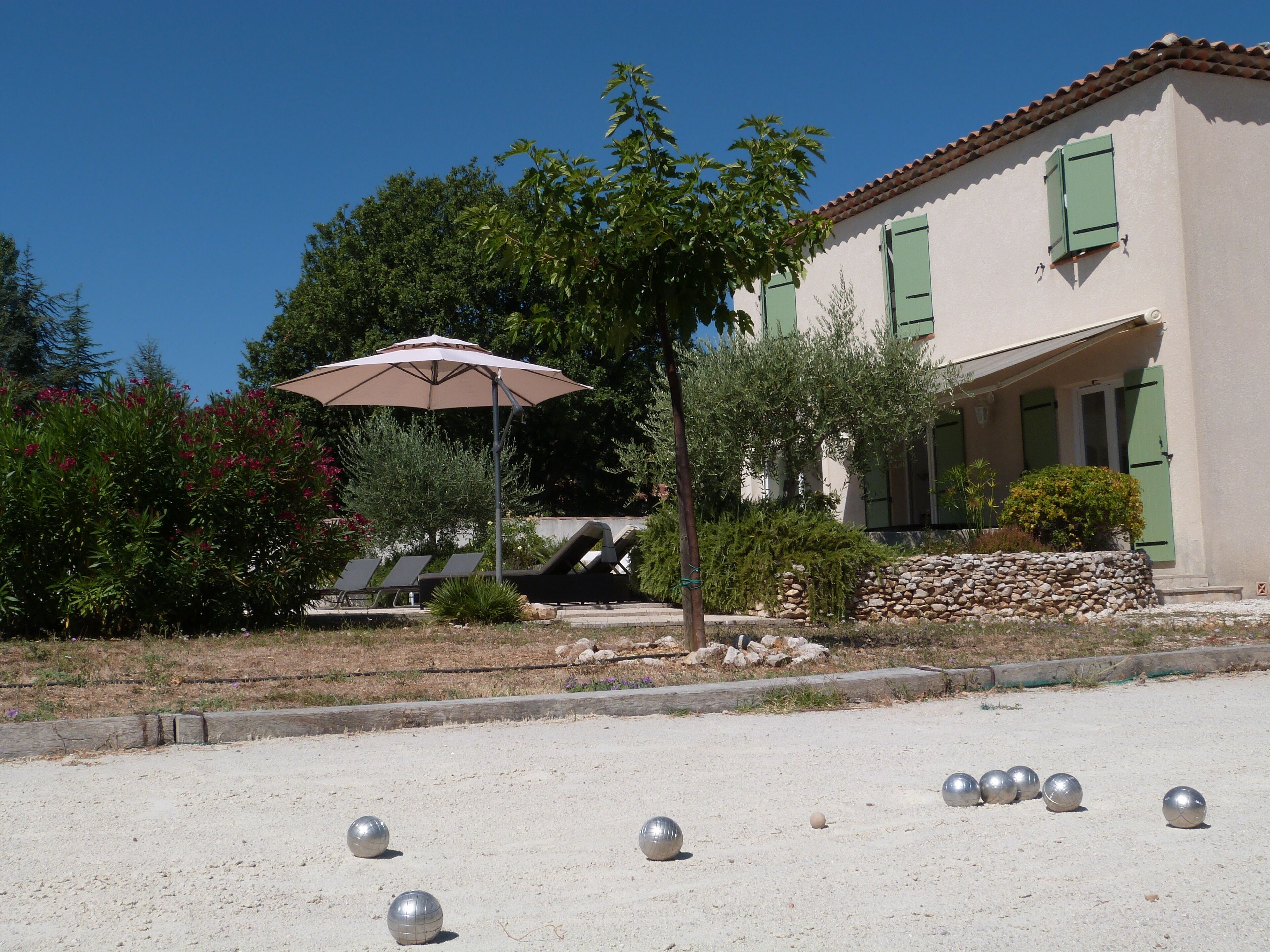 A building with a stone wall, a patio with sun loungers, and a row of metallic balls.