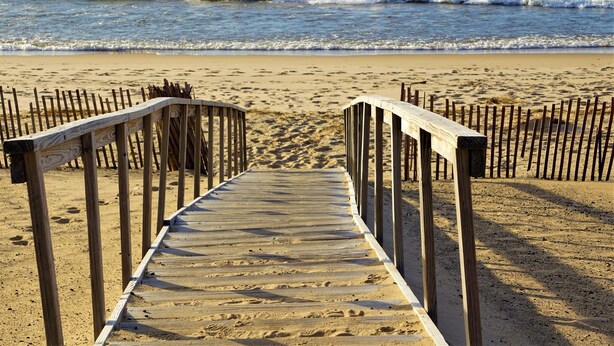 A wooden boardwalk leading to the beach with a wooden fence on either side.