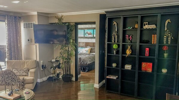 A living room with a sofa, a TV, a bookshelf, and a bed.