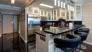 A modern kitchen with a central island, stainless steel appliances, and bar stools. - Direct Oceanfront in the Heart of Waikiki! Spectacular New Custom Reno! (Honolulu)