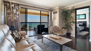 A spacious living room with a large sofa, a coffee table, and a view of the ocean through floor-to-ceiling windows. - Direct Oceanfront in the Heart of Waikiki! Spectacular New Custom Reno! (Honolulu)