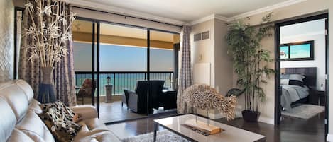 A spacious living room with a large sofa, a coffee table, and a view of the ocean through floor-to-ceiling windows.