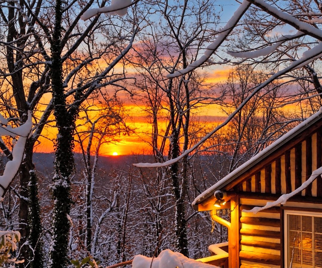 Eine Blockhütte mit Blick auf einen Sonnenuntergang über verschneiter Landschaft.