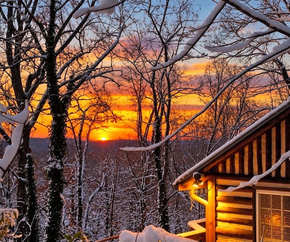 Una cabaña de troncos con vista a un atardecer sobre un paisaje nevado.