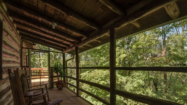Un porche de madera con mecedoras y vistas a un bosque.