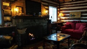 Interior acogedor de una cabaña de madera con chimenea, un sofá rojo y un televisor montado en la pared.