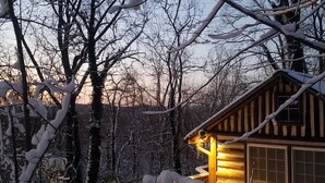 Una cabaña de troncos con luz cálida, rodeada de árboles cubiertos de nieve.