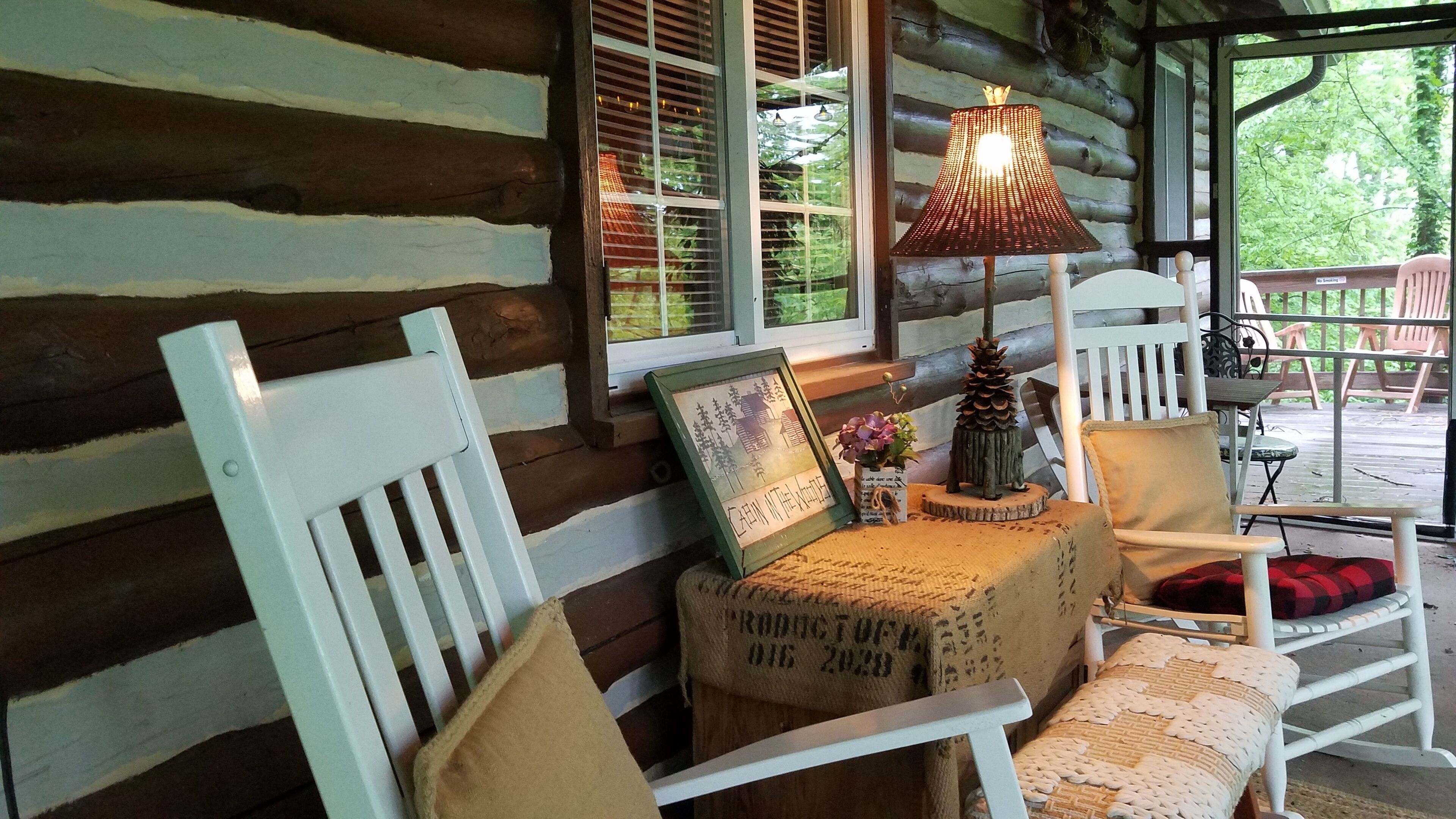 A cozy cabin interior with a wooden bench, a table with a lamp, and a framed picture on the windowsill.
