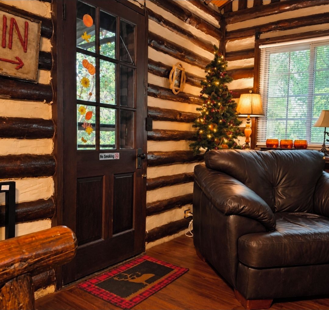 L’intérieur d’une cabane en rondins, avec un canapé en cuir, un sapin de Noël et une porte sur laquelle est apposée une pancarte « Interdiction de fumer ».