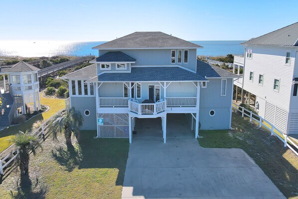 A two-story beachfront house with a balcony, a covered porch, and a view of the ocean.