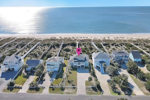 An aerial view of a coastal residential area with houses, a beach, and a pier.