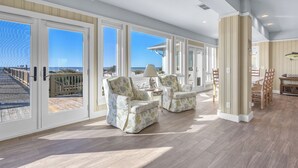 Una habitación amplia con grandes puertas correderas de vidrio que dan a un balcón, un ventilador de techo y un comedor con sillas y mesa de madera.