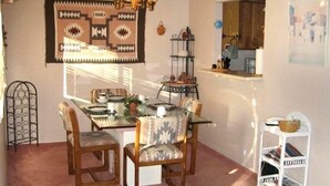 A dining area with a table set for four, surrounded by chairs with patterned upholstery. A chandelier hangs above the table, and a wall-mounted shelf with kitchen items is visible to the right. - Sedona Red Rock Private Casita (sedona)