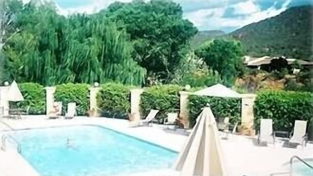A swimming pool with lounge chairs and umbrellas, surrounded by lush greenery and mountains in the background. - Sedona Red Rock Private Casita (sedona)