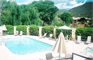 Piscina com espreguiçadeiras e guarda-sóis, cercada por vegetação exuberante e montanhas ao fundo.