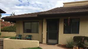 A house with a well-maintained lawn, a porch with two chairs, and a small garden area with a potted plant. - Sedona Red Rock Private Casita (sedona)