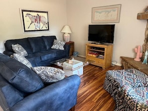 A living room with a sofa, a coffee table, a TV on a wooden stand, and a patterned ottoman. - Sedona Red Rock Private Casita (sedona)