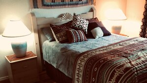 A bedroom with a bed, two bedside tables, two lamps, a patterned wall hanging, and a wooden floor. - Sedona Red Rock Private Casita (sedona)