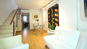 Una sala de estar moderna con una escalera, un comedor y un cuadro abstracto grande.