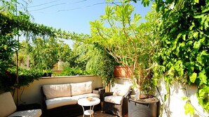 Un área de estar al aire libre acogedora, con un sofá, sillas y una pequeña mesa, rodeada de abundante vegetación y una planta en maceta.