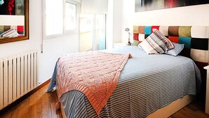 Un dormitorio con cama, radiador, ventana y mesita de noche con lámpara.