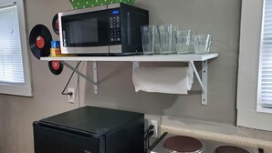 Keittiössä on mikroaaltouuni, Haier-merkkinen jääkaappi ja liesi. Seinällä on vinyylilevyjä ja vihreä, valkoisin pistein kuvioitu kangas.