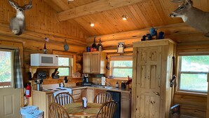 L’intérieur de la cabane est en bois et comprend une table à manger avec des chaises, un coin cuisine avec un four à micro-ondes et une cheminée.