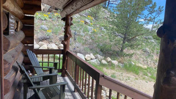 Une cabane en bois dotée d’une véranda, de fauteuils Adirondack et offrant une vue sur une colline rocheuse parsemée d’arbres.