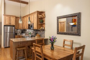 Une cuisine avec des meubles en bois, un réfrigérateur en acier inoxydable, un îlot central avec des tabourets et une table à manger avec des chaises.